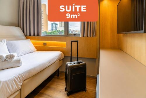 a hotel room with a suitcase next to a bed at Linked Batel Curitiba by Xtay in Curitiba