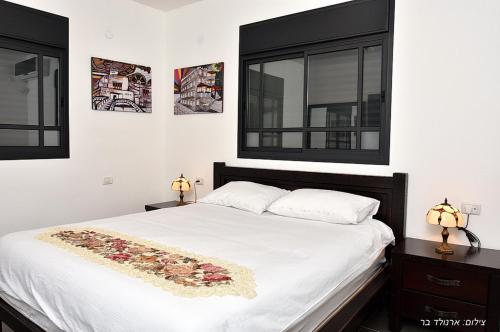 a bedroom with a white bed with two windows at מקום טוב באמצע במושבת כנרת in Kinneret