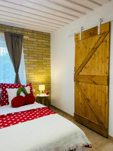 a bedroom with a wooden door and a bed with red pillows at VarázsLakos Birtok in Tázlár