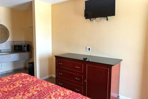 a bedroom with a bed and a dresser with a tv on the wall at Great Western Inn Pasadena in Pasadena