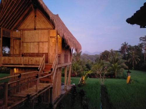 a wooden house with a grass roof in a field at Aska Bamboo House in Tampaksiring