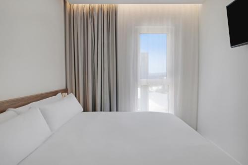 a white bedroom with a large bed and a window at B&B HOTEL Murcia Thader in Churra