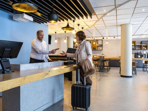 a man and a woman with a suitcase standing at a counter at Ibis Namur Centre in Namur