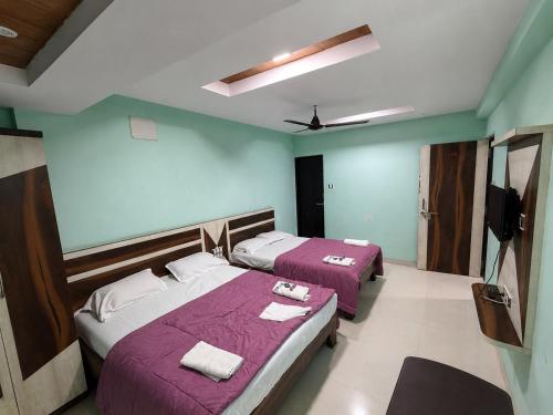 a bedroom with two beds with purple blankets and a tv at Sunset View in Mahabaleshwar