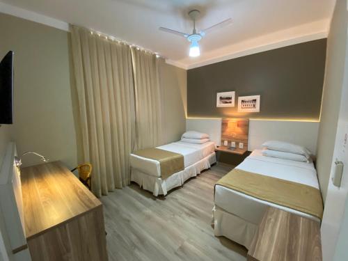 a hotel room with two beds and a desk at JB Palace Hotel in Divinópolis