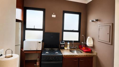a kitchen with a stove and a sink and two windows at Flat em Hotel com Estacionamento Grátis e Piscina in Santos