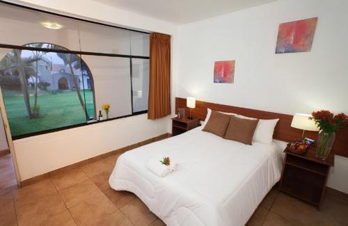 a bedroom with a white bed and a large window at El Angolo Chosica in Nicolas de Pierola