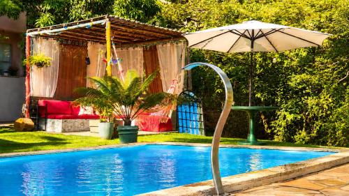 a swimming pool with an umbrella and a table at Villa Pella - Chalé Rosa- hidro e café manhã in Brumadinho
