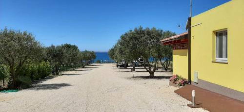 a dirt road with a yellow building and trees at Relax Camp Pitches in Pakoštane