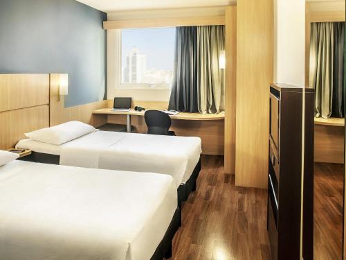 a hotel room with two beds and a desk at Ibis Belo Horizonte Savassi in Belo Horizonte