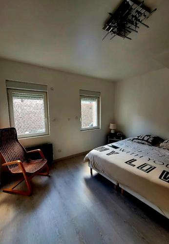 a bedroom with a bed and a chair and two windows at La Ch'tite Maison in Masnières