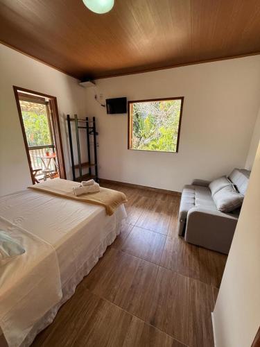 a bedroom with a bed and a couch and two windows at Agradável Kitnet próximo à Praia do Forte in Mata de Sao Joao