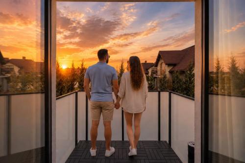a man and woman standing on a balcony watching the sunset at Apartamenty Racławicka Mszczonów in Mszczonów