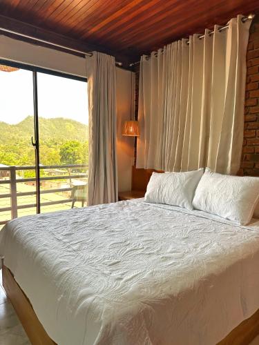 a bedroom with a white bed with a large window at Altura525 hotel in Jarabacoa