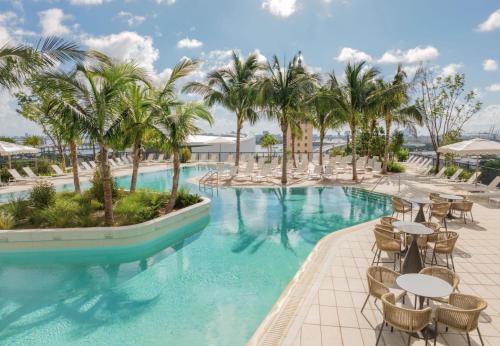 a resort pool with tables and chairs and palm trees at Luxury Penthouse Best Price ,Breathtaking Balcony Views, Ocean & City, Resort Pool, Spa, Gym, in Miami