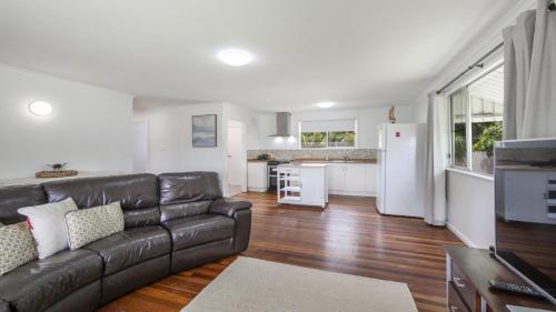 a living room with a leather couch and a kitchen at Twin Palms Retreat in Wooli