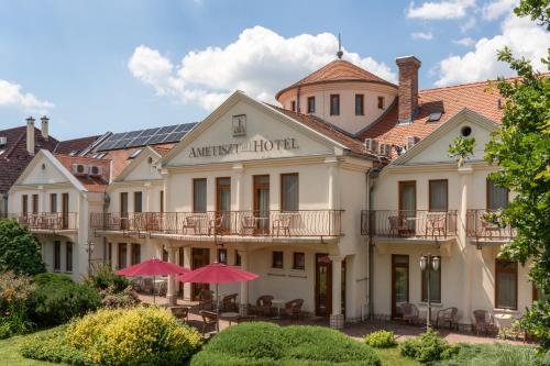 a hotel with tables and umbrellas in front of it at Ametiszt Hotel Harkány in Harkány