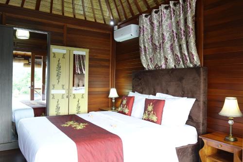 a bedroom with two white beds and wooden walls at Puri Karang Besakih in Menanga