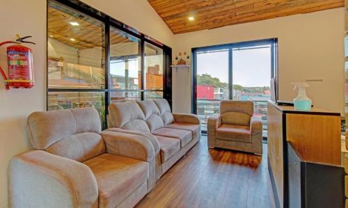 a living room with a couch and chairs and windows at Green Woods Cottage by JN in Mahabaleshwar