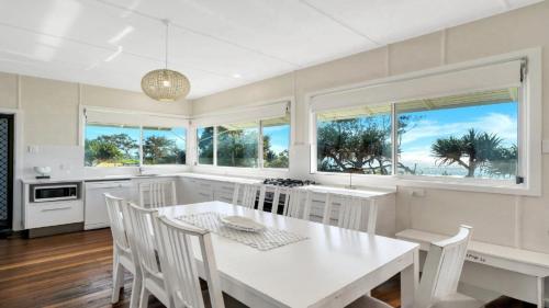 a kitchen with a white table and chairs and windows at Frangipani Cottage in Wooli