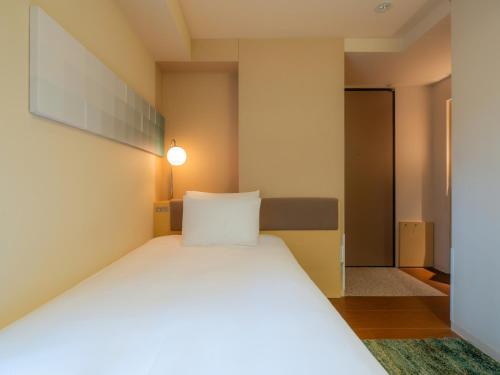 a bedroom with a white bed with a light on the wall at Hotel Resol Ikebukuro in Tokyo