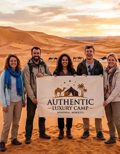 a group of people holding a sign in the desert at Authentic Luxury Camp in Merzouga