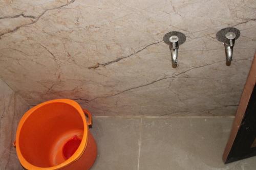 an orange toilet in a bathroom with two faucets at Srivari Lodge in Arcot