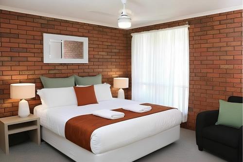 a bedroom with a large bed and a brick wall at Jacaranda Apartments in Swan Hill