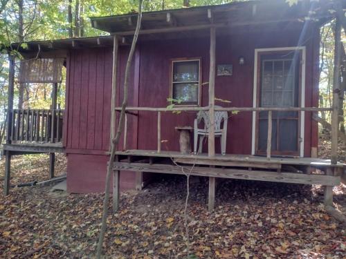 a red cabin in the woods with a chair on the porch at Thunder Ridge Cabins B&B - Wolf Den in Rockbridge