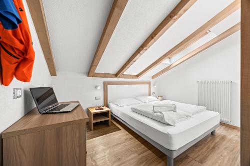 a bedroom with a bed and a laptop on a desk at Aparthotel Des Alpes in Cavalese