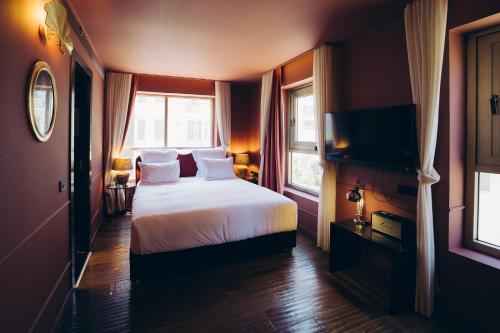 a bedroom with a bed and a tv and windows at Casa Suzanna Hotel in Tel Aviv