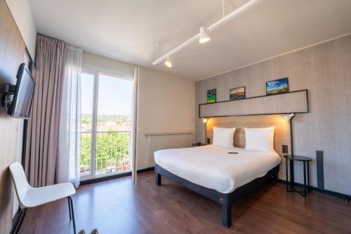 a hotel room with a bed and a large window at Ibis Centre Millau in Millau