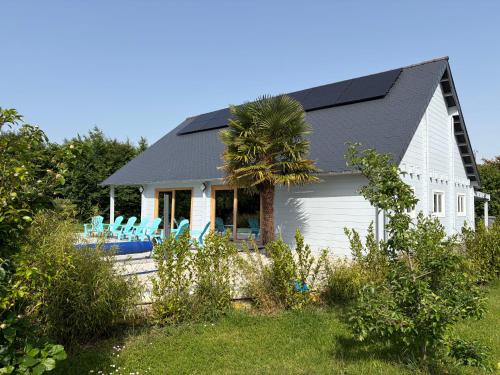 a white house with a palm tree and chairs at Gîte Ker Koad in Pluduno