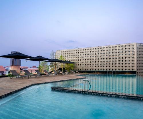 a swimming pool with chairs and umbrellas in front of a building at U Nimman Chiang Mai in Chiang Mai