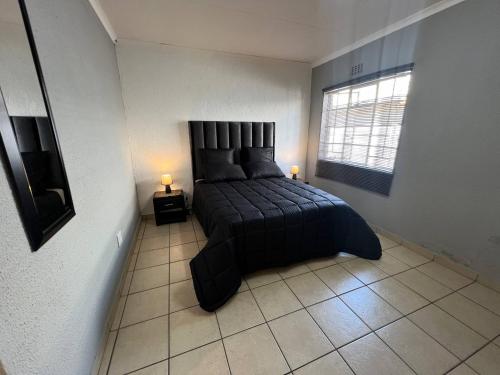 a bedroom with a bed with a black bedspread and a window at Stylish 1-Bed Cottage,Garden, Pool Secure Parking in Alberton
