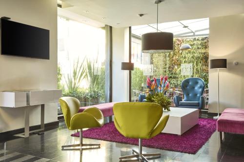 a living room with yellow and blue chairs and a tv at Hotel bh Parque 93 in Bogotá