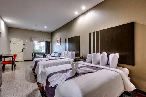 a hotel room with four beds with white sheets at Humble Inn & Suites in Humble