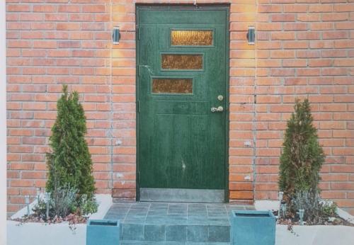 a green door on a brick building with two bushes at Lägenhet nära hallstaberg & centrum in Sollefteå