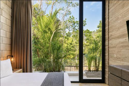 a bedroom with a large window with a view of trees at Hum Living Luxury Villas in Tulum