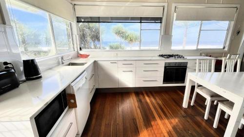 a kitchen with white cabinets and a table and windows at Frangipani Cottage in Wooli