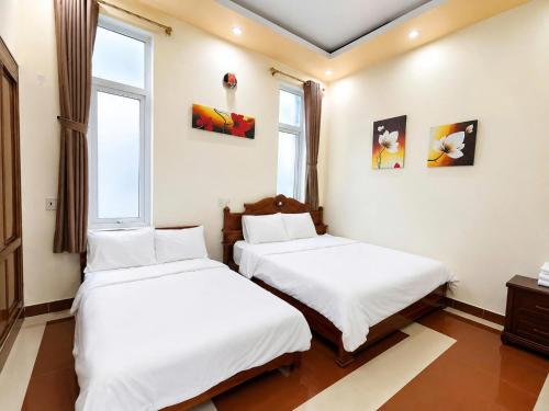 two beds in a room with two windows at The Mellow House Nhật Lệ in Dong Hoi