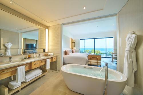 a bathroom with a tub and a bedroom with a bed at Halekulani Okinawa in Onna