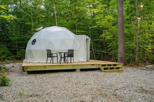 a tent with chairs and a table in the woods at Pleasant River Glamping Dome 3 King bed in Bethel