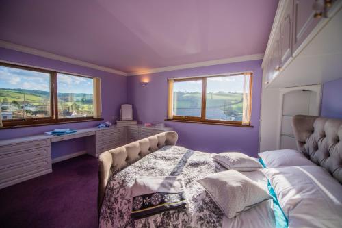 1 dormitorio con paredes de color púrpura, 1 cama y ventanas en Y Grange, en Llanfihangel-y-creuddyn