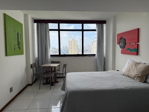 a bedroom with a bed and a table and a window at Vitória Marina Flat in Salvador
