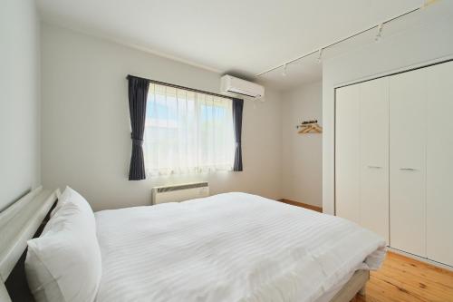 a bedroom with a white bed and a window at Suzuran Haus in Higashikawa