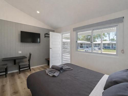 a bedroom with a bed and a desk and window at Lakeside Forster Holiday Park in Forster