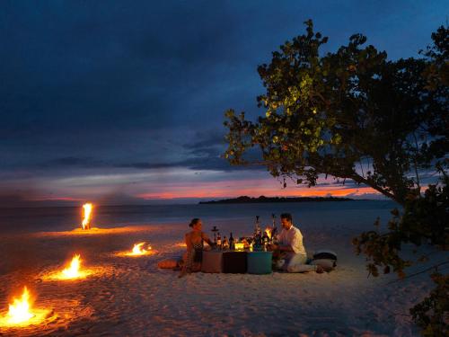 a group of people sitting around a table on a beach with fires at Cocoon Maldives - All Inclusive in Lhaviyani Atoll