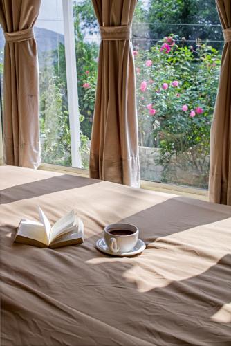 a book and a cup of coffee on a bed with a window at Bhimtaal cottages in Bhīm Tāl