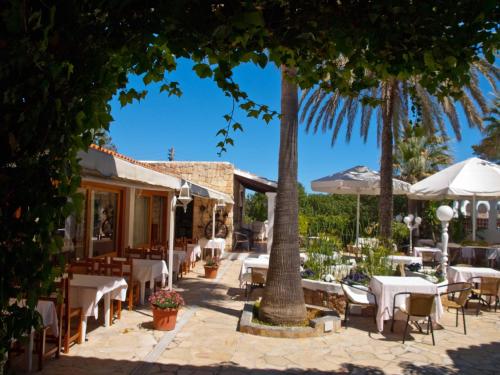 een restaurant met tafels en stoelen en palmbomen bij Hotel Club Can Jordi in Cala Llenya